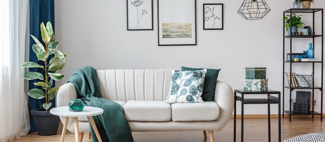 Black table next to sofa with green blanket in cozy apartment interior with gallery of posters